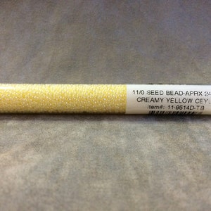 May include: A clear plastic tube filled with 11/0 seed beads in a creamy yellow color. The label reads "11/0 SEED BEAD-APRX 24-GMS CREAMY YELLOW CEYLON Item#: 11-9514D-TB".