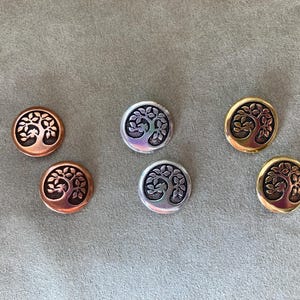 May include: Six round metal buttons featuring a tree of life design. The buttons are available in three colours: silver, gold, and copper.