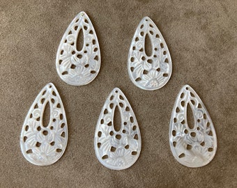May include: Five white mother of pearl teardrop shaped pendants with intricate floral designs and a hole at the top for hanging.