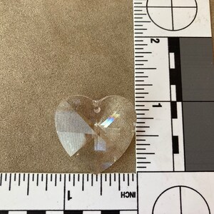 May include: A clear crystal heart-shaped prism with a hole at the top for hanging. The prism is about 1 inch in size.