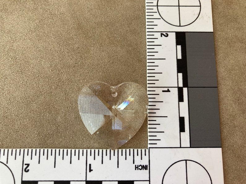 May include: A clear crystal heart-shaped prism with a hole at the top for hanging. The prism is about 1 inch in size.
