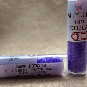 May include: Two small clear plastic tubes filled with purple seed beads. The label on the tube on the left reads "Item#: DB783-TB DELICA BD DYED MATTE TRANSP PURPLE-APRX 7.2GM". The label on the tube on the right reads "MIYUKI 11/0 DELICA OD".