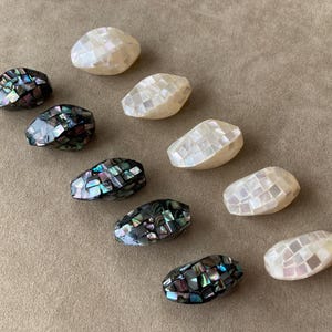 May include: A collection of ten oval-shaped beads arranged in two columns. Five beads feature a white iridescent mother-of-pearl mosaic tile pattern, while the other five beads display a dark, multi-colored iridescent abalone shell mosaic finish.