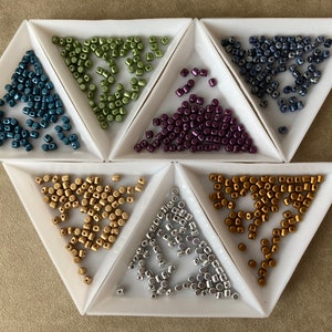 May include: Six triangular trays filled with small, round beads in various colours, including teal, green, purple, gold, and silver.