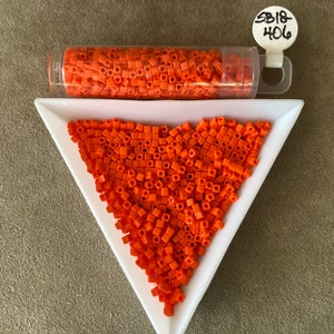 May include: Orange square beads are displayed in a clear tube and a white triangular dish. The beads are a vibrant orange color. The tube has a white tag with the text "SB18-406". These beads are likely used for crafting or jewelry making.