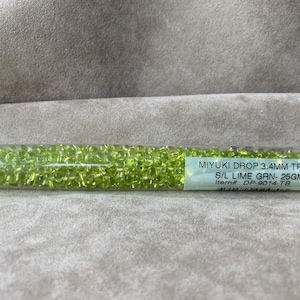 May include: A clear plastic tube filled with lime green Miyuki Drop beads. The label reads "MIYUKI DROP 3.4MM TRANS S/L LIME GRN - 25GM Item#: DP-9014-TB".
