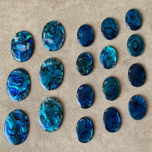 Puede incluir: Una colección de 20 cabujones ovalados de concha de abulón. Las conchas son iridiscentes con tonos de azul, verde y negro.