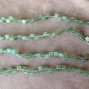May include: A strand of green glass beads with a white geometric pattern. The beads are strung on a clear thread and are arranged in a curved line.