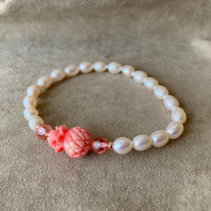 May include: A white pearl bracelet with a pink carved pineapple charm and crystal accents.