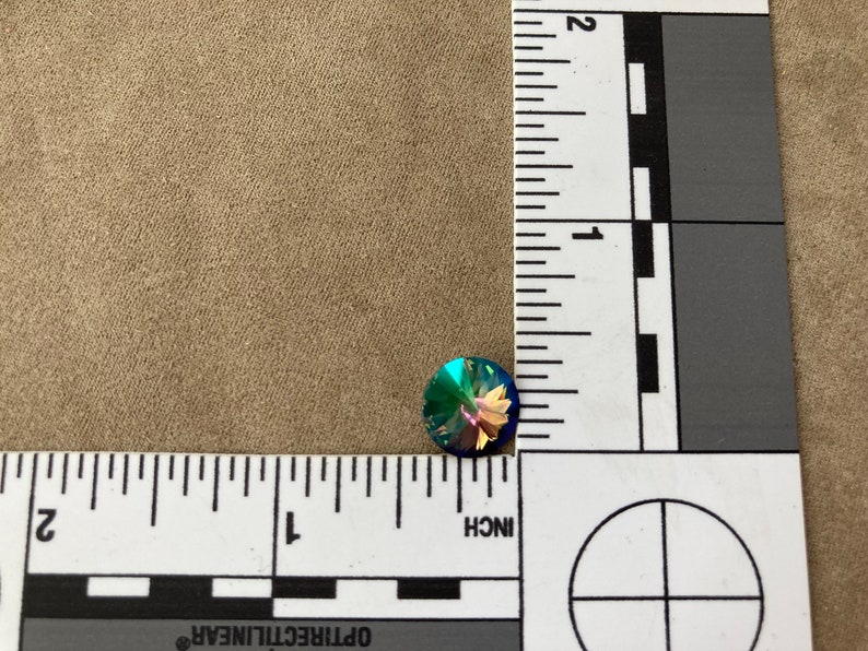 May include: A single iridescent blue, green, and purple round rhinestone with a faceted surface.