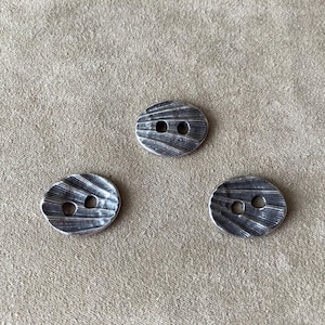 Può includere: Tre bottoni argentati con un designo testurizzato e rigato. Ogni bottone ha due fori.