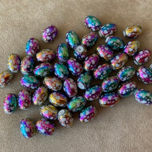 May include: A large group of oval-shaped iridescent beads with white hearts printed on them. The beads are a mix of colors, including pink, purple, blue, green, and gold.