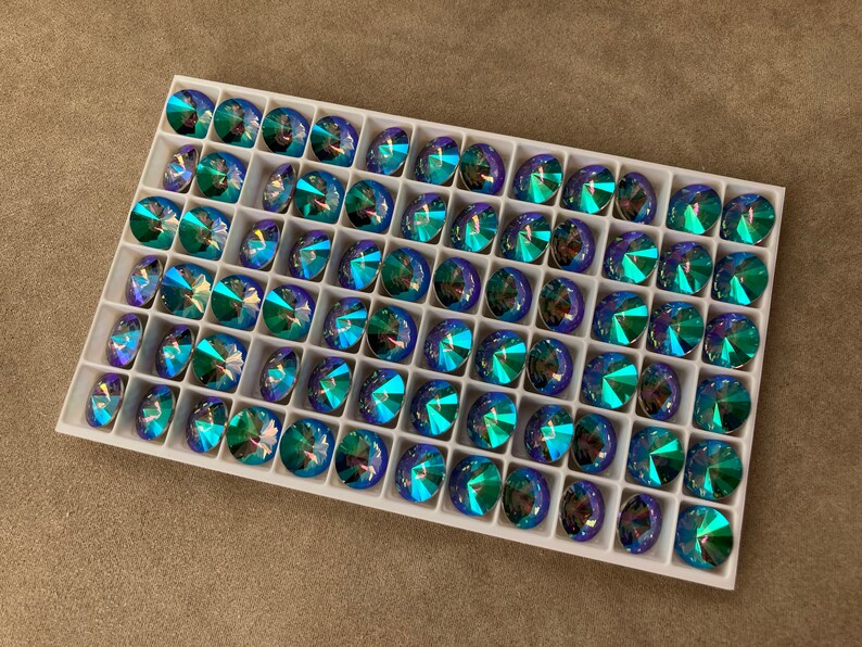 May include: A white tray filled with 49 blue and green iridescent glass rhinestones.