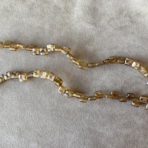 May include: Two strands of brown and white square beads. The beads have a mottled pattern.