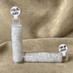 May include: Two small clear plastic containers filled with iridescent white beads. The containers have labels that read "SB18 A50".