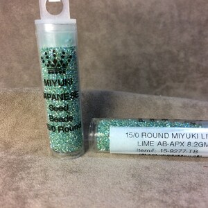 May include: Two clear tubes filled with small, light green seed beads. One tube has a label that reads "MIYUKI JAPANESE Seed Beads 5/0 Round." The other tube has a label that reads "15/0 ROUND MIYUKI LINED LIME AB-APX 8.2GM."