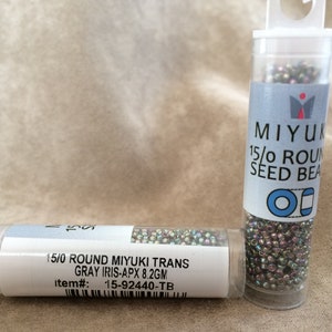 以下が含まれることがあります： 銀色のビーズが詰まった透明なプラスチック製の小さなチューブが2本。チューブには、「15/0 Round Miyuki Trans Gray Iris-APX 8.2GM Item#: 15-92440-TB」と「Miyuki 15/0 Round Seed Beads」のラベルが貼られています。