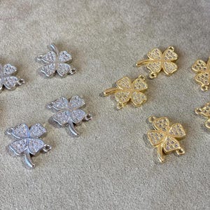 May include: A collection of silver and gold four-leaf clover charms with clear crystal accents. The charms are perfect for jewelry making or adding a touch of luck to your crafts.