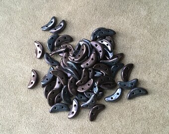 May include: A pile of dark blue and iridescent crescent-shaped glass beads. The beads have two holes in each.