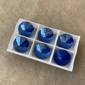 May include: Six blue iridescent round rhinestones in a white plastic container.