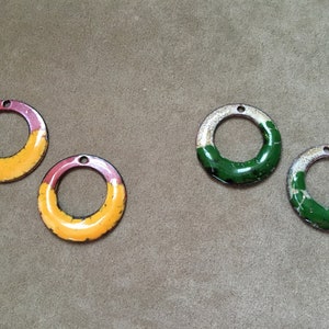 May include: Four round metal charms with a hole at the top. Two charms are yellow and red with a white ring in the center. Two charms are green and white with a white ring in the center.