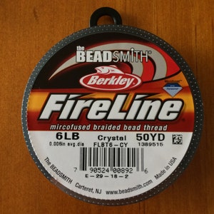 May include: A spool of black FireLine microfused braided bead thread by Berkley. The spool is labeled with the text "FireLine", "mircofused braided bead thread", "6LB", "0.006in avg.dia", "Crystal", "FLBT6-CY", "50YD", "1389515", "The BEADSMITH", "Carteret, NJ", "www.beadsmith.com", and "Made in USA".