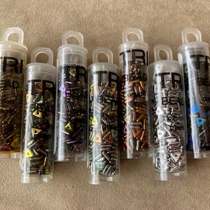 May include: Eight small clear plastic containers filled with colorful triangle-shaped beads. The containers are labeled "Tri Bead Czech Glass".