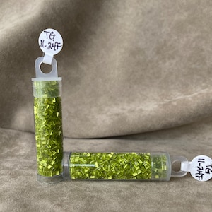 May include: Two small clear tubes filled with green seed beads. The tubes have white labels with the text "TG 11-24TF" on them.
