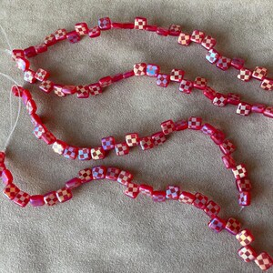May include: Four strands of red and gold checkered glass beads. The beads are square shaped and strung on clear thread.