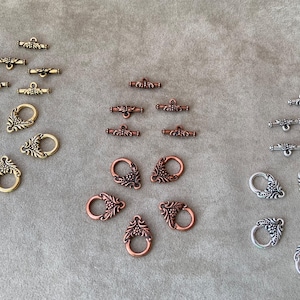 May include: Assortment of ornate metal toggle clasps in silver, copper, and gold tones. Each clasp features a decorative floral design.