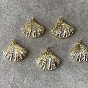 May include: Five gold-tone shell-shaped pendants with clear crystal accents. Each pendant has a loop at the top for attaching to a chain or cord.