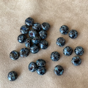 May include: A collection of 20 black and blue ceramic beads with white speckles. The beads are round and have two holes in each.