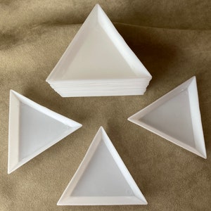 May include: Four white triangular trays, one stacked on top of the other, on a brown fabric surface.