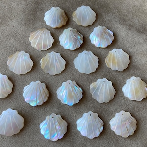 May include: A collection of iridescent white seashell pendants, each with a scalloped edge and a small hole for stringing. The shells are arranged on a neutral-toned surface, showcasing their natural beauty and potential for jewelry making or craft projects.