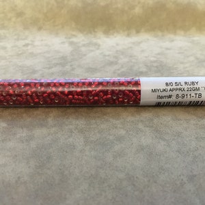 May include: A clear plastic tube filled with red seed beads. The label reads "8/0 S/L RUBY MIYUKI APPRX 22GM "UBE Item#: 8-911-TB"