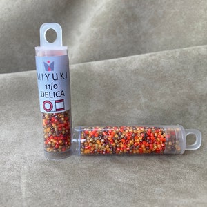 May include: Two small clear tubes filled with colorful seed beads. The tubes are labeled "MIYUKI 11/0 DELICA".