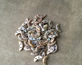 May include: A pile of light brown and white ceramic crescent moon shaped beads. The beads have a speckled, iridescent finish.