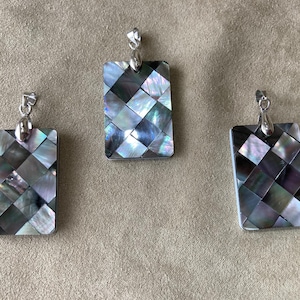 May include: Three silver pendant necklaces with black and white mother of pearl inlay. The pendants are rectangular and have a geometric pattern.