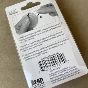 May include: A white rectangular product packaging for a thread waxer by Basic Elements and The Beadsmith. The back of the card features a black and white diagram showing how to use the tool, along with instructions in English, French, and Spanish.