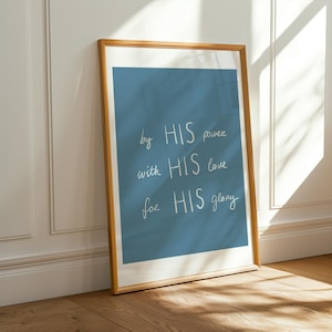 Puede incluir: Una impresión enmarcada con un fondo azul y una escritura blanca que dice "by HIS power with HIS love for HIS glory." El marco es de color marrón claro y está apoyado contra una pared blanca y un suelo de madera.