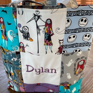 May include: A patchwork tote bag with a Nightmare Before Christmas theme. The bag is made of different fabrics with various characters from the movie, including Jack Skellington and Sally. The bag has a white panel with the name "Dylan" embroidered in purple.