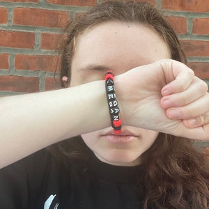 May include: A black beaded bracelet with red spacers and the name "Megan" spelled out in white letters.
