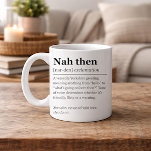 May include: A white ceramic mug featuring black printed text that defines the Yorkshire exclamation Nah then. The text includes a phonetic pronunciation, a definition of the greeting, and a list of related phrases including ey up, alright love, and steady on.