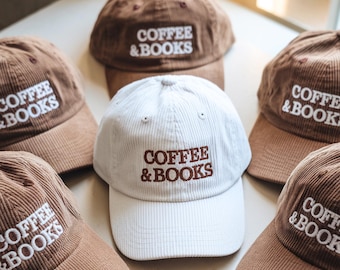 May include: A collection of corduroy baseball caps in shades of brown and white. Each cap features the embroidered text "COFFEE & BOOKS" in a contrasting color. The caps are arranged in a visually appealing display, showcasing their design.
