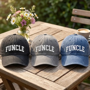 May include: Three baseball caps in black, charcoal gray, and denim blue, each featuring the word "FUNCLE" embroidered in white capital letters across the front panel. The caps have a structured crown, a curved brim, and a distressed fabric finish.