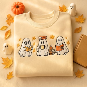 Puede incluir: Sudadera color crema con un dise&ntilde;o bordado de tres fantasmas de dibujos animados leyendo libros, con hojas de oto&ntilde;o y una calabaza. Los fantasmas llevan gafas y sostienen tazas de caf&eacute;. Un dise&ntilde;o con tem&aacute;tica oto&ntilde;al.