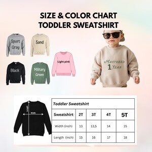 Op de afbeelding: Maat- en kleurenkaart voor peuter sweatshirts. De kaart toont sweatshirts in sportgrijs, zand, zwart, legergroen en lichtroze. Een kind draagt een zandkleurig sweatshirt met "MASTERED 1 YEAR" erop gedrukt. Afmetingen in inches.