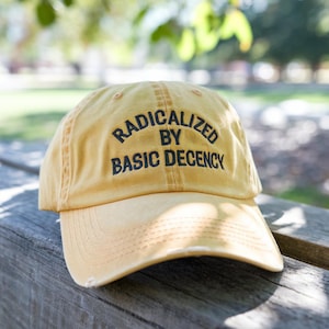 May include: A yellow baseball cap with the text "Radicalized by Basic Decency" embroidered in black.
