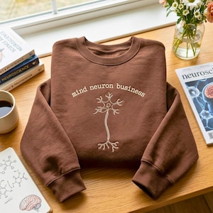 以下が含まれることがあります： 「mind neuron business」という白い刺繍文字と、神経細胞の線画が施された茶色のクルーネックトレーナー。長袖で、襟元、袖口、裾はリブ編みになっています。