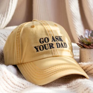 May include: A yellow baseball cap with black stitching and the text "GO ASK YOUR DAD" embroidered on the front.